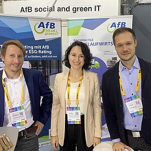 Three employees of AfB standing in front two advertising posters presenting the services and supplies of AfB at the exhibition area of the 57th symposium procurement and logistics at STATION in Berlin.